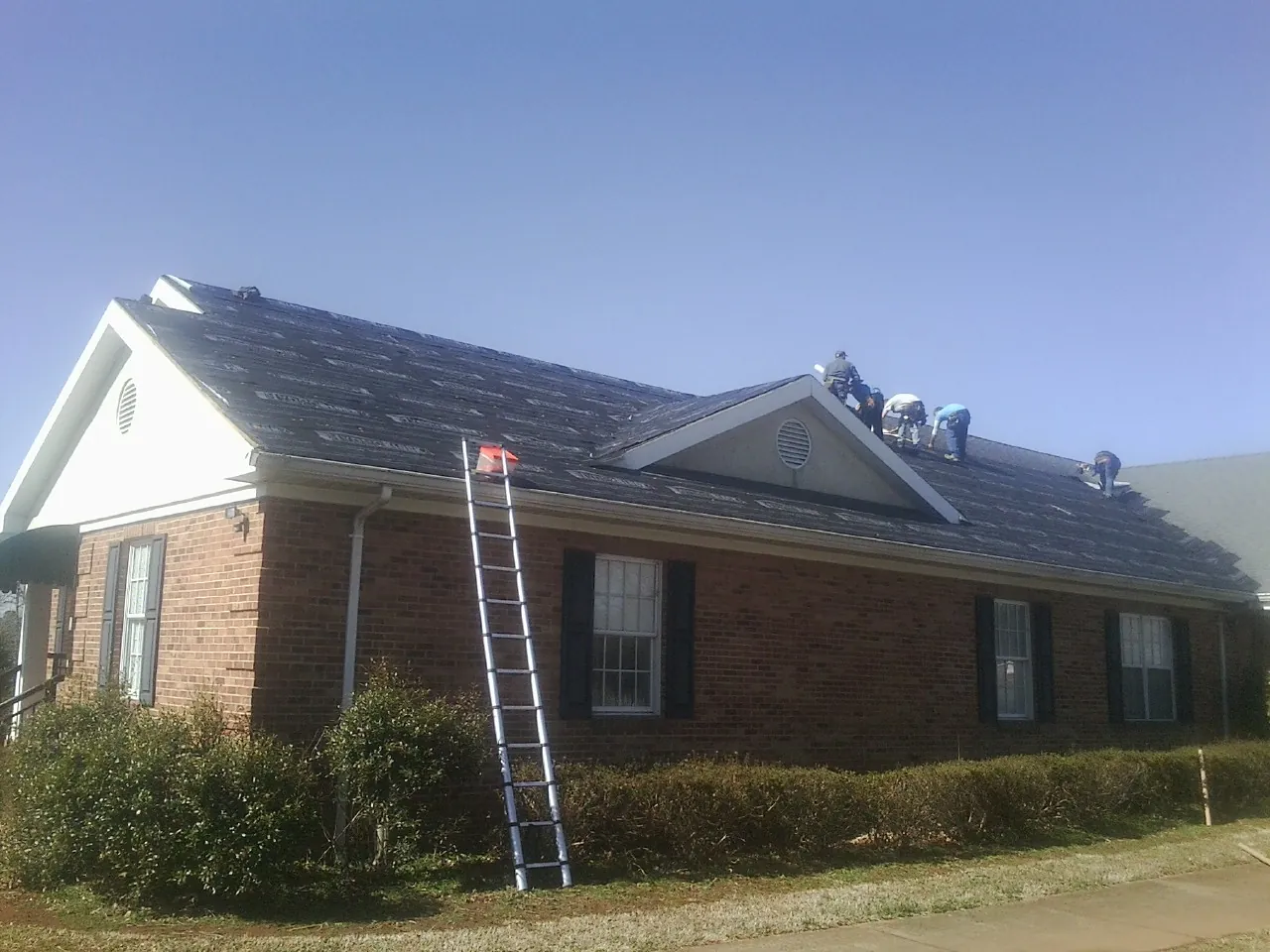 Crew tearing shingles off a brick ranch roof with a ladder set — Emergency Roof Repair work by our crew in Tulare