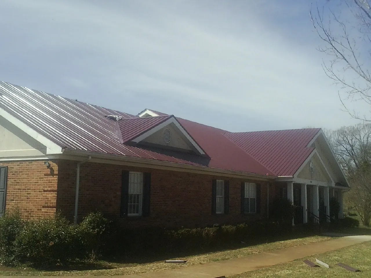 Red metal roof with gabled entries on a long brick building, from a Hail Damage Roof Repair job in Tulare