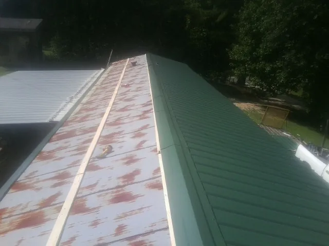 Old rusted panels beside newly installed green metal roofing — Wind Damage Roof Repair by Roofing Brothers in Tulare