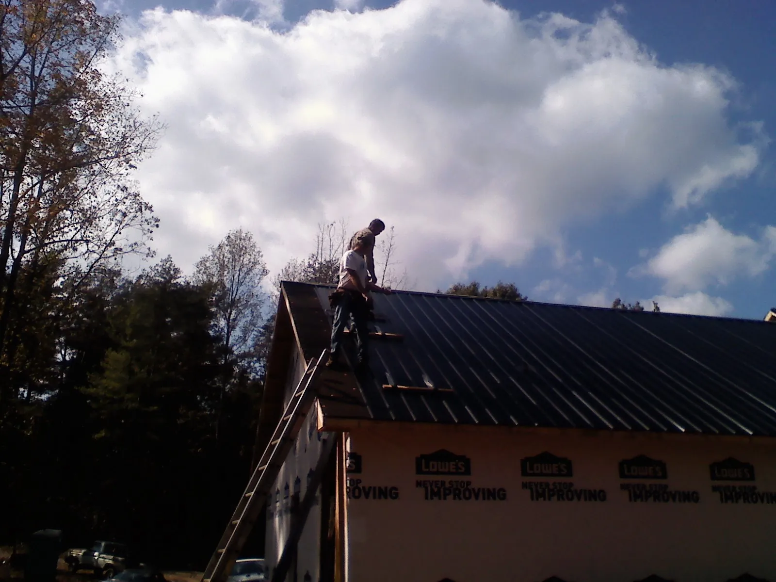 Roofer fastening dark metal panels high against a cloudy sky, from a Roof Inspection job in Tulare