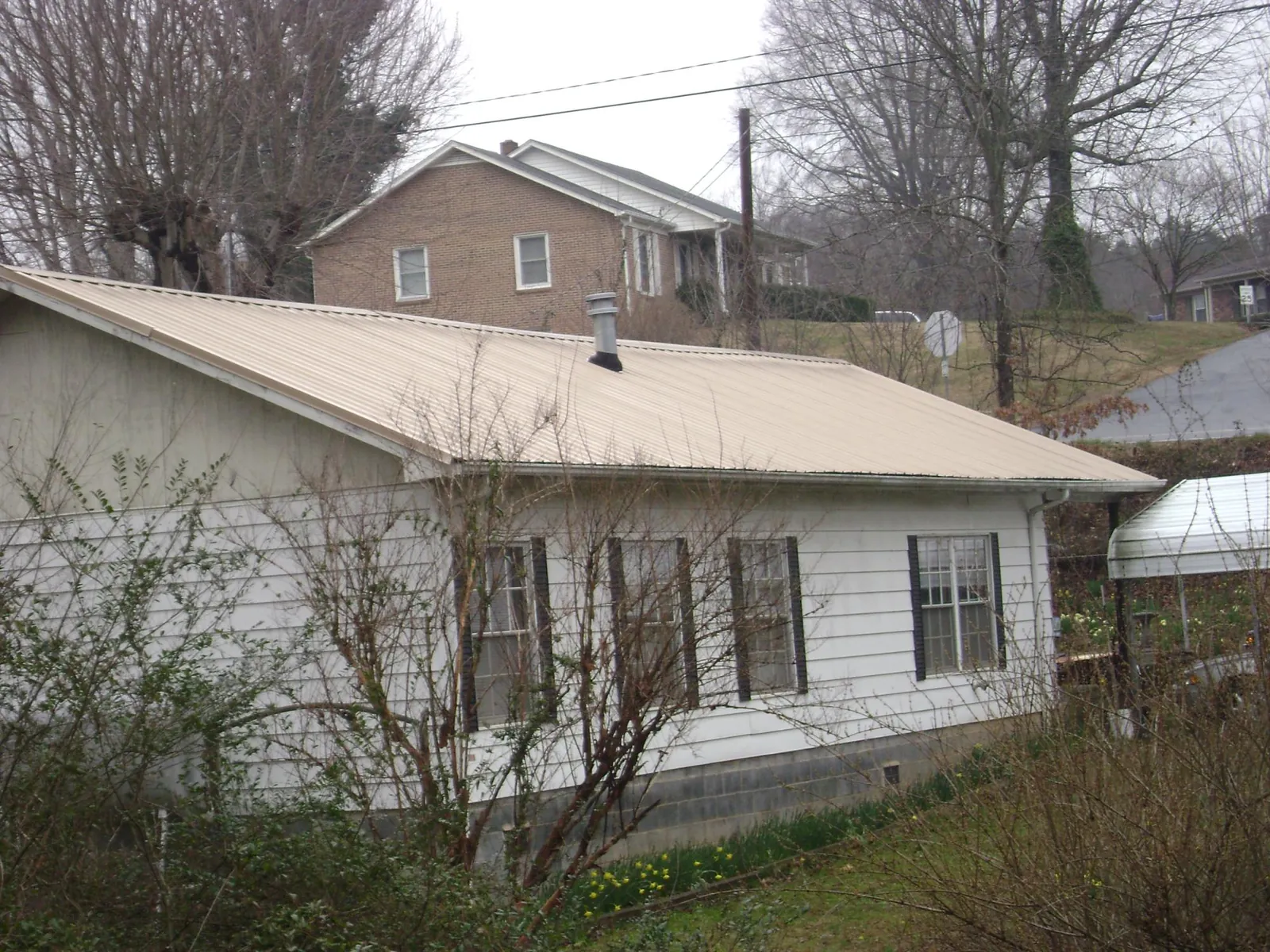 Tan metal roof on a white sided house set into a hillside — Commercial Roofing by Roofing Brothers in Tulare