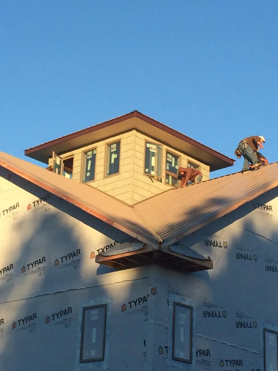 Roofers working around a rooftop cupola on a new metal roof at sunset — Roof Waterproofing in Tulare by Roofing Brothers